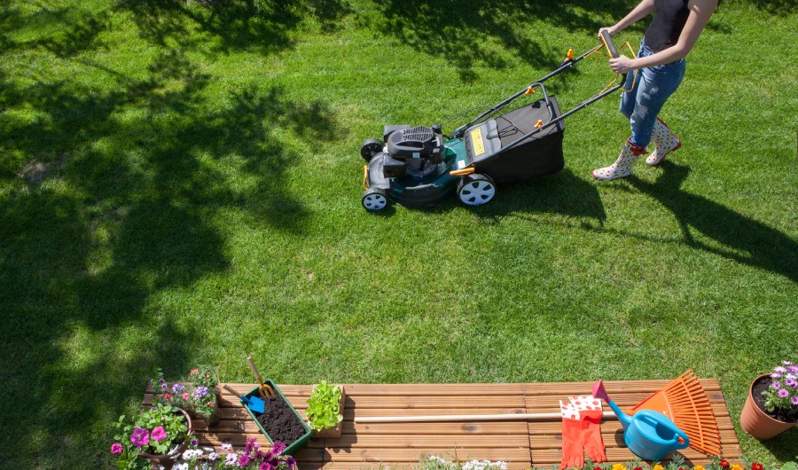 Woman wearing wellington boots mowing grass with lawn mower in the garden