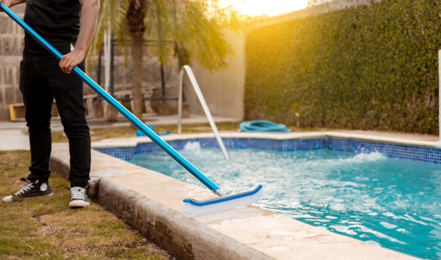 Manos de trabajador limpiando una piscina con cepillo especial, Persona de mantenimiento limpiando piscina con escoba. Limpieza de piscina con escoba